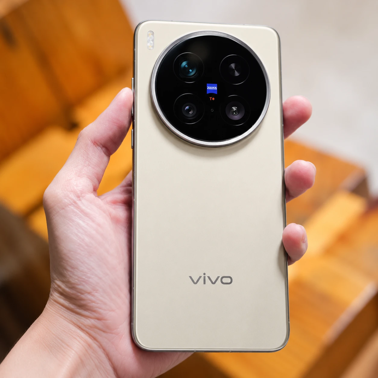 Mano sosteniendo celular Vivo X300 de diseño dorado con cámara circular.